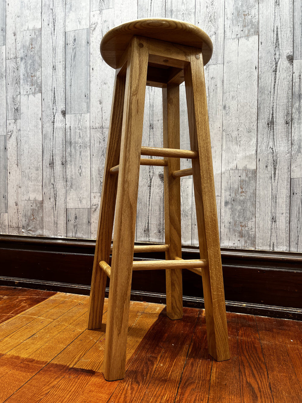 Handmade oak bar stool against a rustic wood wall